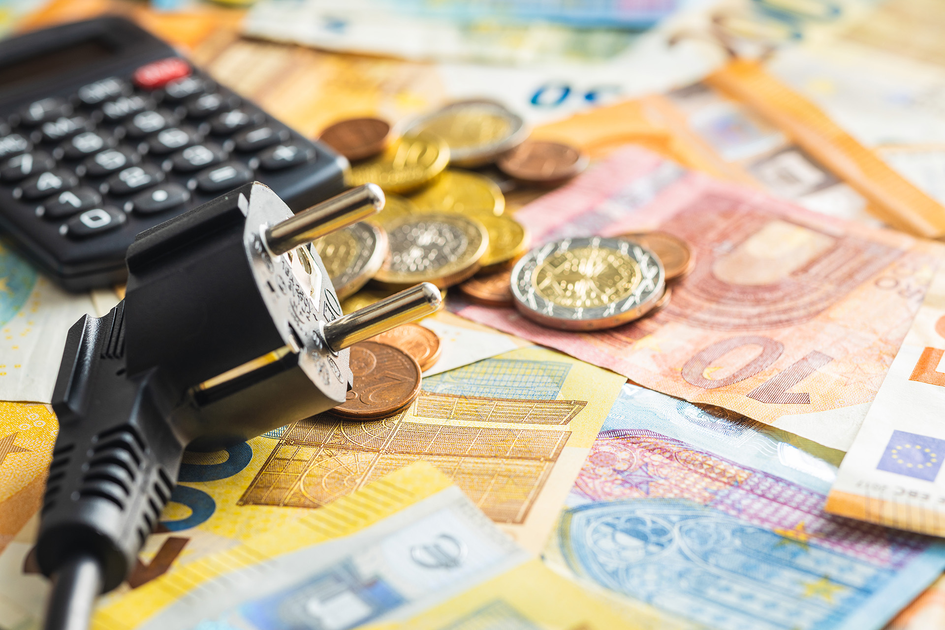 Euronoten und -Münzen quer verteilt auf einer flachen Oberfläche, dazu ein Taschenrechner und ein herausgezogener Stromstecker